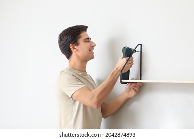 Young Man Installing Modern Shelf In Room