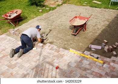 Young man installing paver bricks for large patio, paving backyard