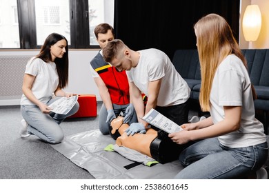 Young man instructor helping to make first aid heart compressions with dummy during the group training indoors.