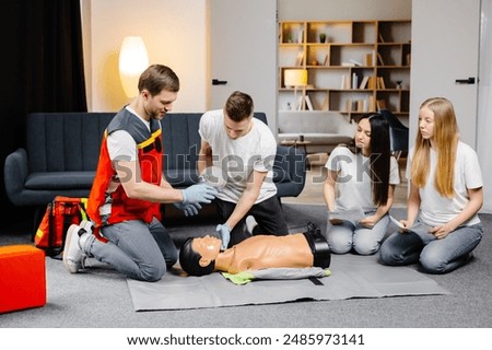 Young man instructor helping to make first aid heart compressions with dummy during the group training indoors.