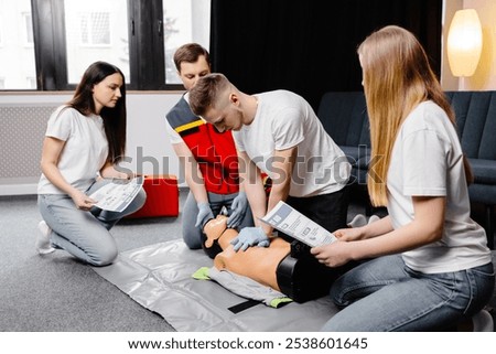 Young man instructor helping to make first aid heart compressions with dummy during the group training indoors.