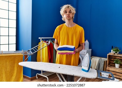 Young man ironing clothes at home puffing cheeks with funny face. mouth inflated with air, catching air.  - Powered by Shutterstock