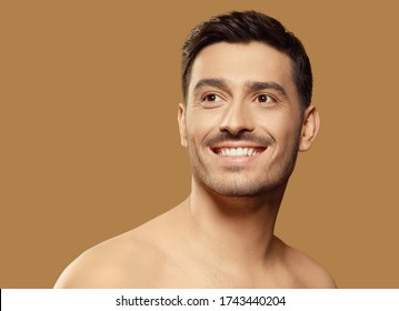 Young Man Isolated On Light Brown Background, Standing In Front Of Camera, Looking Aside As If Aspiring For Good With Happy Smile On Face. Men Beauty Skin Care Concept