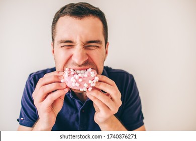 Young man isolated over background. Guy biting pink donut piece with pleasure. Hungry person divour meal. Portrait of glutton.
