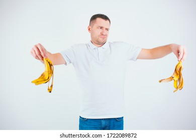 Young Man Isolated Over White Background. Mean Unhappy Guy Hold Banana's Skin In Hands. Want To Throw It Away. Organic Waste.