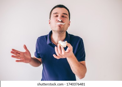 Young Man Isolated Over White Background. Eating Tasty Delicious Fat Small Cake. Part Of Cream Is On His Nose And Face. Yummy Pleasure.