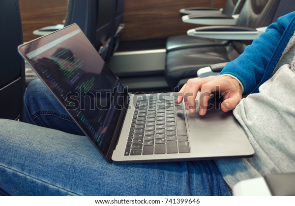 Young man in jeans uses laptop for  writing\
software code in transport. Close\
up.
