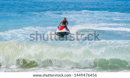 Young man of jet ski rider performs on the waves with much splashes
