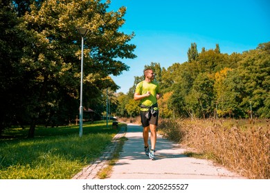 Young Man Jogging In The Green City Park Trail. Full Length Image, Copy Space