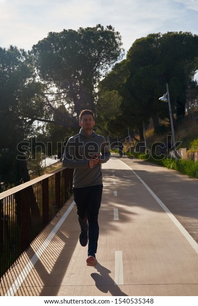 Young man jogging on a path with tall trees in\
the background