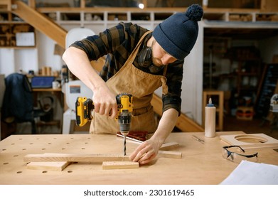 Young man jointer working with drill leaning over table at carpentry workshop - Powered by Shutterstock