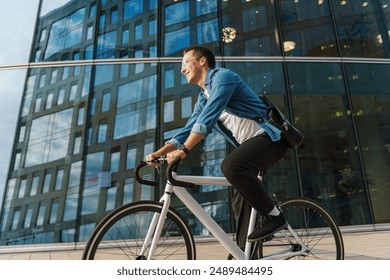 A young man joyfully riding a bicycle past a modern glass office building, embodying a dynamic urban lifestyle.

 - Powered by Shutterstock