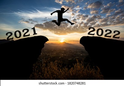 A young man jump between 2021 and 2022 years over the sun and through on the gap of hill  silhouette evening colorful sky. happy new year 2021.