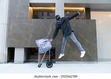 Young Man Jumping In The Air Holding Cart With Large Bazar Bag. The Thrift Shop, Charity, Cleaning Space, Moving, Donation Concept. Wearing Face Mask. Outdoors