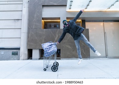 Young Man Jumping In The Air Holding Cart With Large Bazar Bag. The Thrift Shop, Charity, Cleaning Space, Moving, Donation Concept. Wearing Face Mask. Outdoors