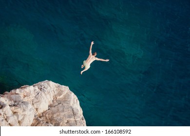 Young Man Jumping From Cliff Into Sea.