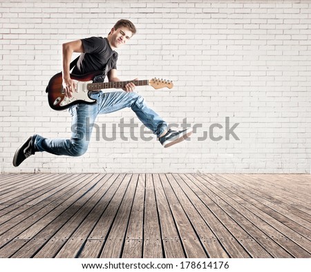 young man jumping with electric guitar on a room