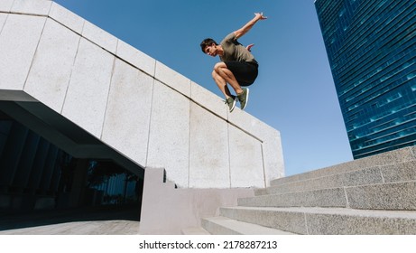 Young man jumping high over steps outdoors. Fit male free runner jumping over stairs in urban space.