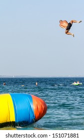 Young Man Is Jumping With Inflatable Water Catapult Balloon On The Sea Shore