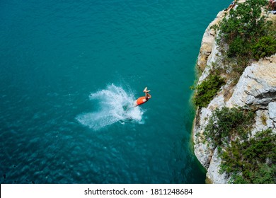 Young man Jumping off a sea Cliff into blue sea