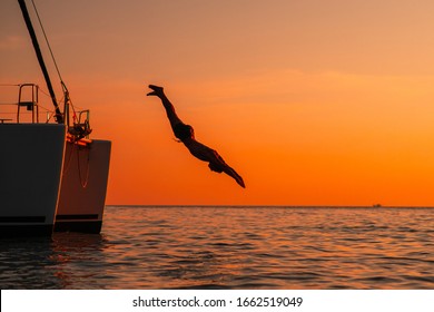 Young man jumping off yacht into water ocean at sunset. Crazy adult guy in swimwear fly from luxury cruise yacht. Summer vacation. Copy space