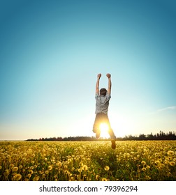 Young Man Jumping On Meadow With Dandelions On Clear Blue Sky Background