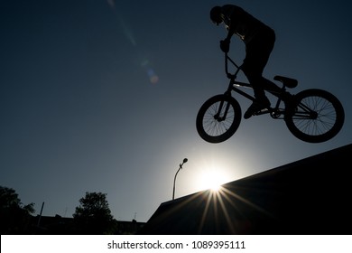 Young Man Jumping And Riding On A BMX Bicycle On A Ramp Over Blue Sky Background