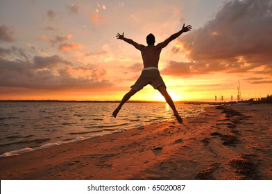 Young man jumping with spread arms celebrating and enjoying the moment at the seaside at sunset