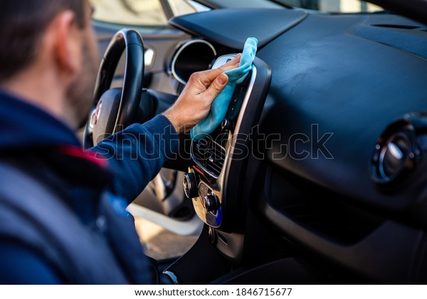 The young\
man is just finishing washing the car. He wipes the plastic parts\
of the car\'s interior with a blue\
cloth.