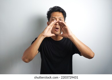 Young Man Keeping Hand Near Mouth And Screaming. Handsome Happy Man Wearing Black T-shirt, Guy Speaking Loudly, Isolated On White Background