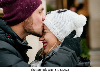 Young Man Kisses Forehead Of Woman In Funny White Winter Hat