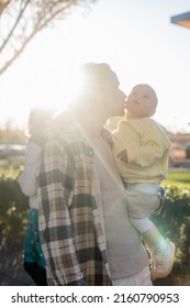 Young Man Kissing Baby Daughter Against Sunlight Outdoors In Treviso