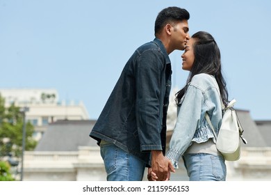 Young man kissing his smiling girlfriend on forehead with love and tender when they are standing outdoors