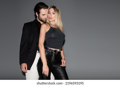 Young Man Kissing Stylish Blonde Girlfriend On Grey Background