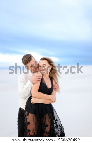 Young man kissing woman in white snowing background in steppe. Concept of winter photi session and romantic love.