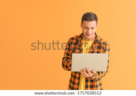 Young man with laptop checking his e-mail on color background