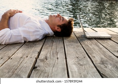 A young man with a laptop laying on a wooden jetty