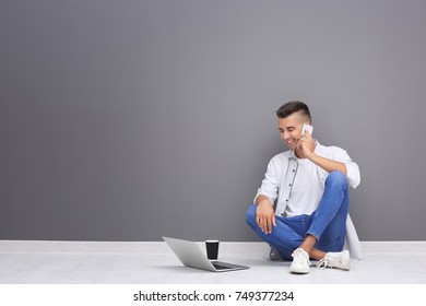 Young man with laptop and mobile phone sitting on floor near grey wall - Powered by Shutterstock