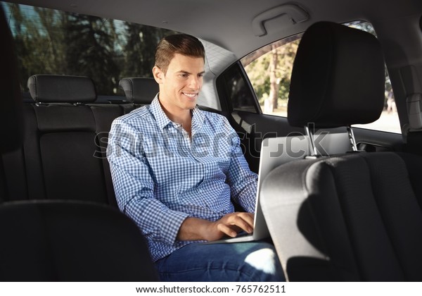 Young man with laptop\
on backseat of car