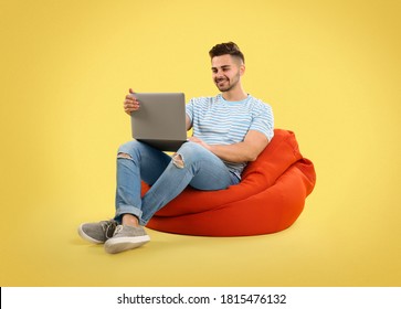 Young Man With Laptop On Bean Bag Chair, Yellow Background