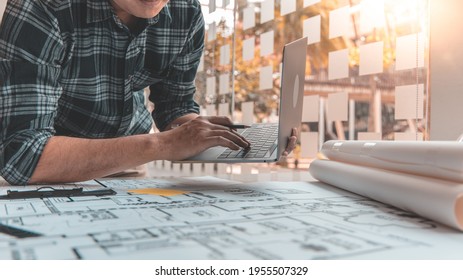Young man with a laptop plotting a system of building structures in blueprints, Architects or engineers are designing buildings using computers to calculate the physical structure to be correct.