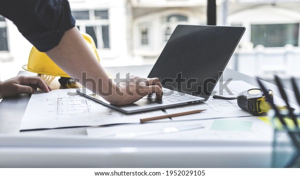 Young man with a laptop plotting a system of
building structures in blueprints, Architects or engineers are
designing buildings using computers to calculate the physical
structure to be correct.