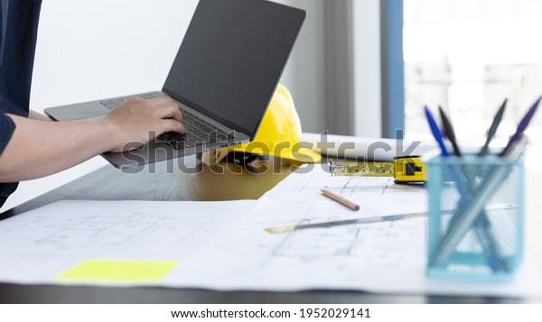 Young man with a laptop plotting a system of
building structures in blueprints, Architects or engineers are
designing buildings using computers to calculate the physical
structure to be correct.