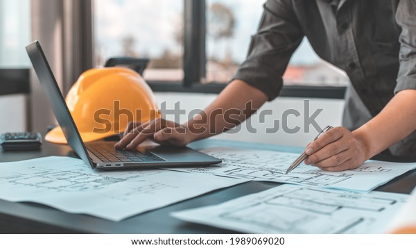 Young man with a laptop plotting a system of\
building structures in blueprints, Architects or engineers are\
designing buildings using computers to calculate the physical\
structure to be correct.