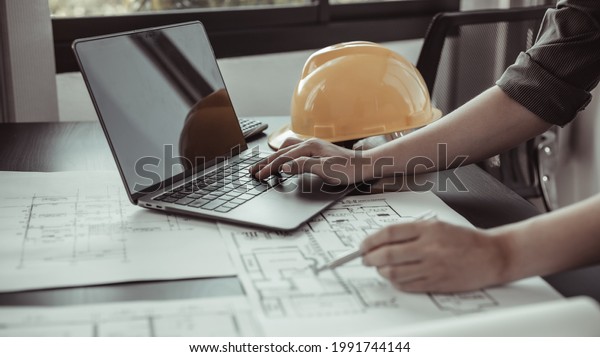 Young man with a laptop plotting a system of\
building structures in blueprints, Architects or engineers are\
designing buildings using computers to calculate the physical\
structure to be correct.