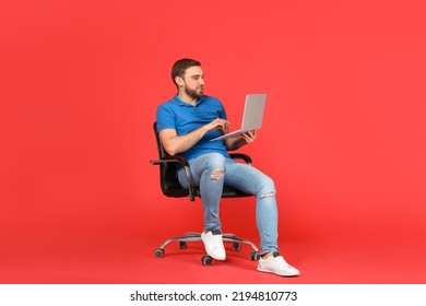 Young Man With Laptop Sitting In Comfortable Office Chair On Red Background