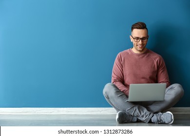 Young Man With Laptop Sitting Near Color Wall