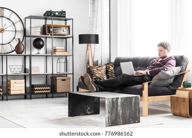 Young Man With Laptop Sitting On The Couch In Black And White Living Room Interior With Industrial Table
