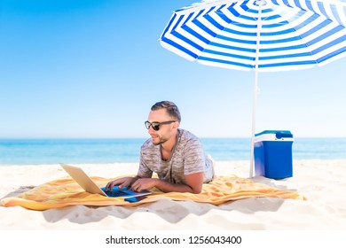 Young Man With Laptop Working On The Sand Beach