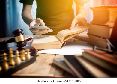 Young man lawyer consulting with teamwork by video conference on mobile and reading a book of lawyer in working desk with sunlight effect in vintage tone of photography.